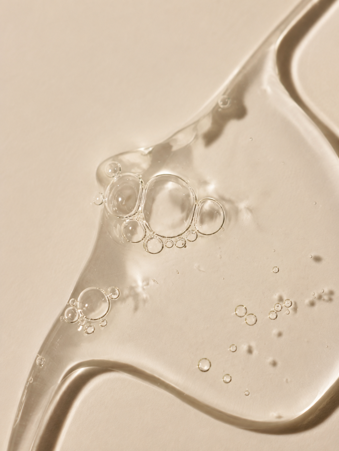 Close-up of a transparent, glossy liquid or gel with small bubbles on a warm beige background.